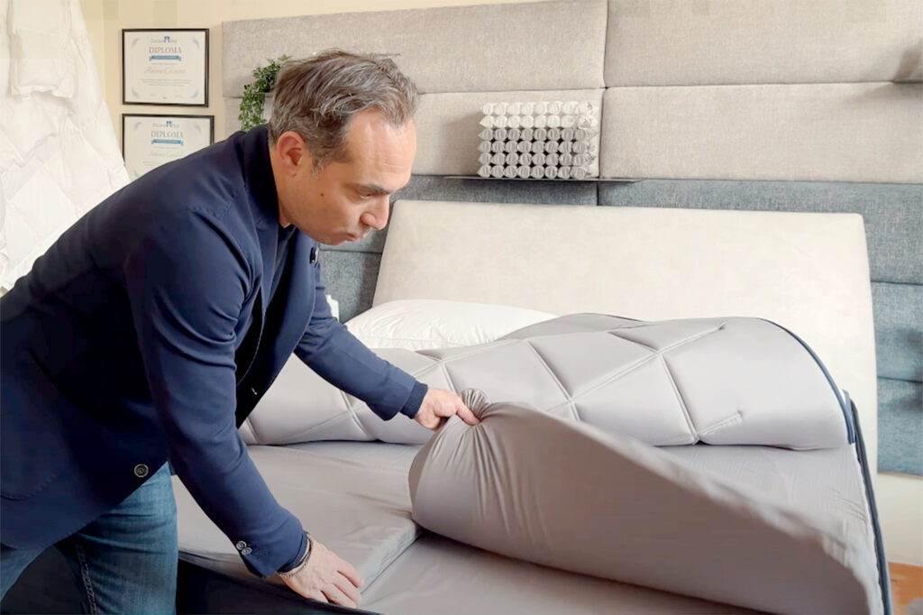 Antonio Chimenti che solleva la fodera del materasso per mostrare un topper singolo in memory foam, posizionato sopra il materasso principale.