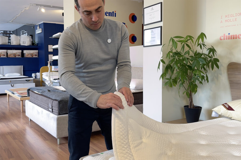 Antonio Chimenti solleva un topper per materasso, mostrando le sue caratteristiche e il materiale che lo compone.